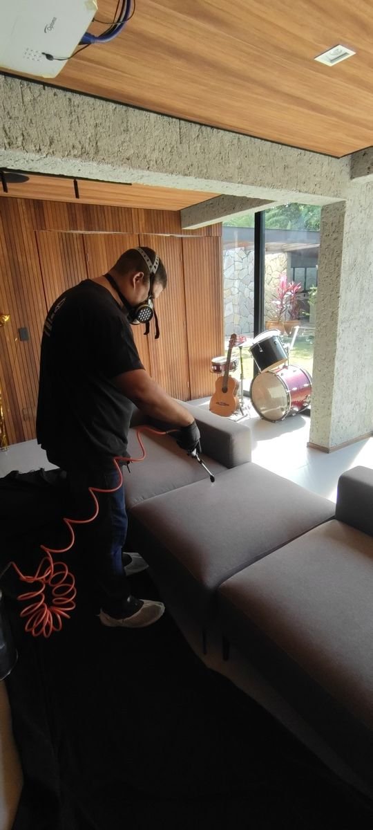 Técnico aplicando produto protetor em sofá cinza em sala de estar